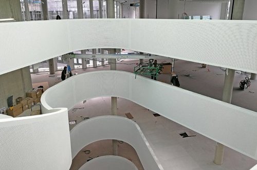 Blick auf ein modernes Firmengebäude im Bau mit geschwungenen weißen Mehrstock-Gängen: Ein SCHILLING-Alu-Portalkran wird im Innenbereich zum Materialtransport eingesetzt.