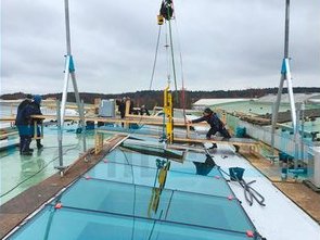Zwei Arbeiter montieren mit einem SCHILLING Aluminium-Portalkran Dachfenster auf dem Flachdach eines Firmengebäudes.