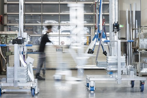 Ein Mann schiebt eine Last auf Rollen durch die Produktion von SCHILLING in Friedrichshafen, im Hintergrund Metallgestelle und großen Fenstern, die Bewegung ist leicht verschwommen dargestellt.