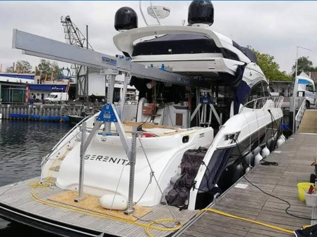 Ein Aluminium-Portalkran von SCHILLING hebt oder hält einen großen Motorbootrumpf in einer Bootswerft zur Durchführung von Wartungsarbeiten über einem Steg.