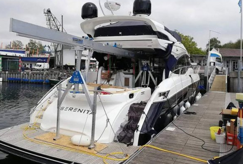 Ein Aluminium-Portalkran von SCHILLING hebt oder hält einen großen Motorbootrumpf in einer Bootswerft zur Durchführung von Wartungsarbeiten über einem Steg.