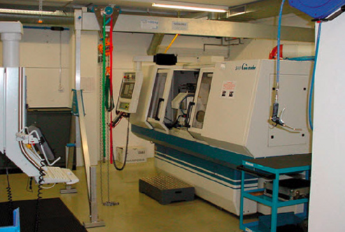 Ein SCHILLING-Alu-Portalkran hebt und transportiert Werkstücke zur Be- und Entladung einer CNC-Maschine in einer Produktionsumgebung.