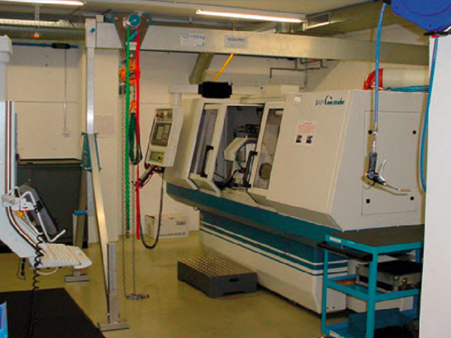 Ein SCHILLING-Alu-Portalkran hebt und transportiert Werkstücke zur Be- und Entladung einer CNC-Maschine in einer Produktionsumgebung.