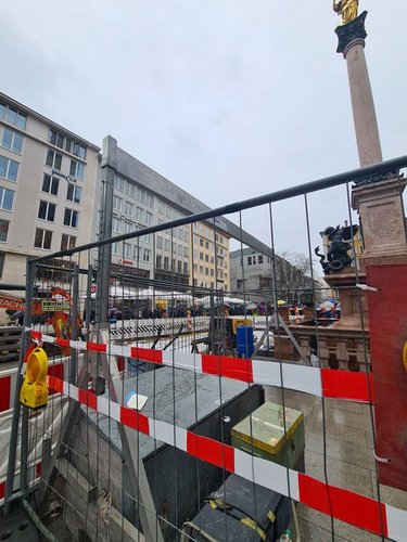 SCHILLING Case Study Alu-Portalkran in München Blick auf eine Baustelle in München mit rotem und weißem Flatterband auf einem Platz mit historischen Gebäuden und einer Säule mit einer goldenen Statue.