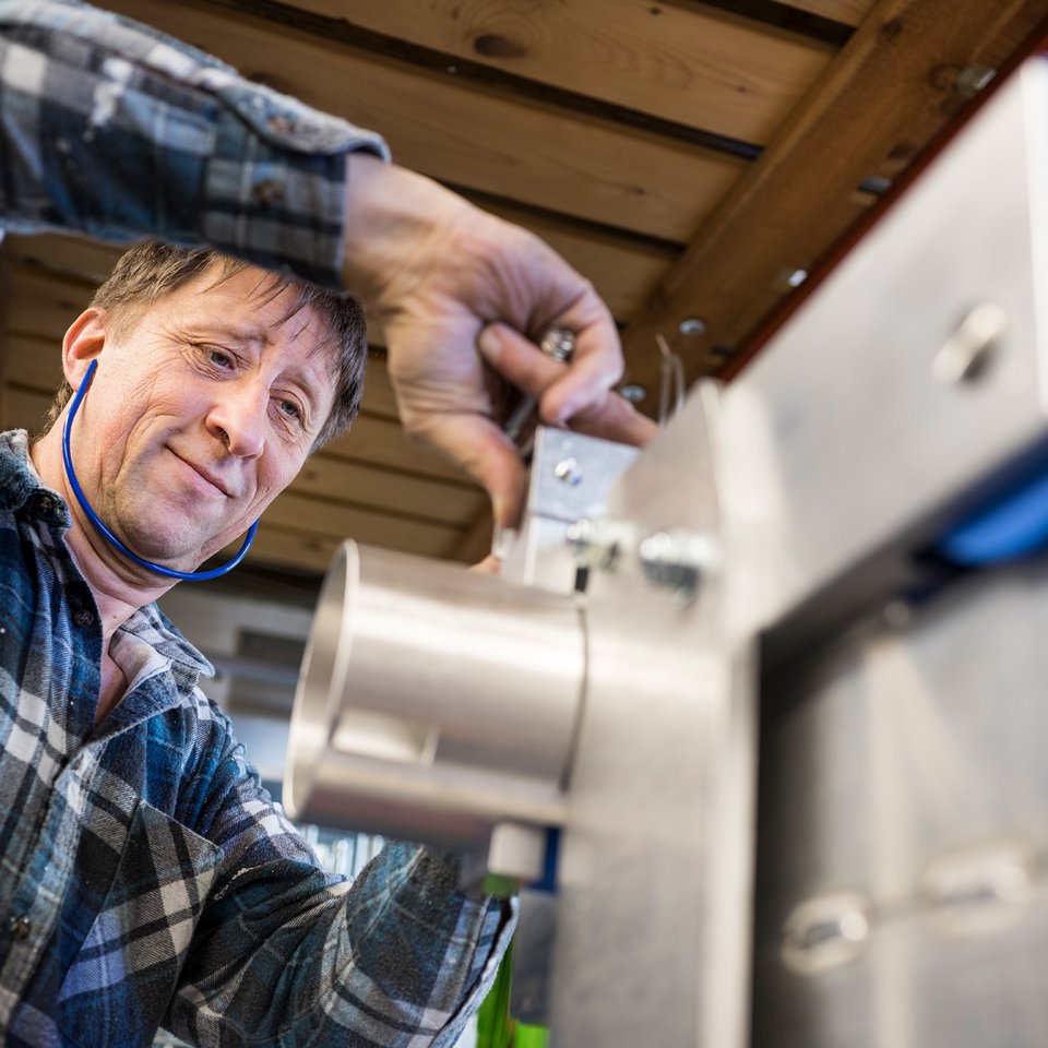 Ein Mitarbeiter von SCHILLING Kran- und Hebetechnik in einem karierten Hemd arbeitet mit Gehörschutz in der Produktion an einer Maschine.