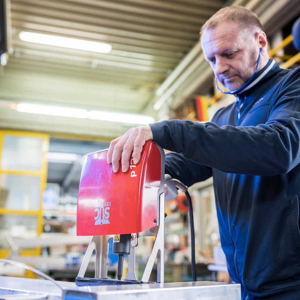 Ein Mann trägt Gehörschutz und bedient konzentriert einen rot lackierte elektrischen Bohrer.
